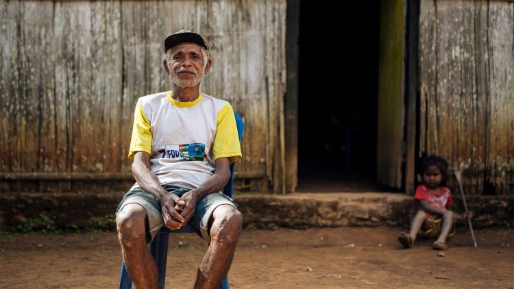 An elderly man sitting outside his home