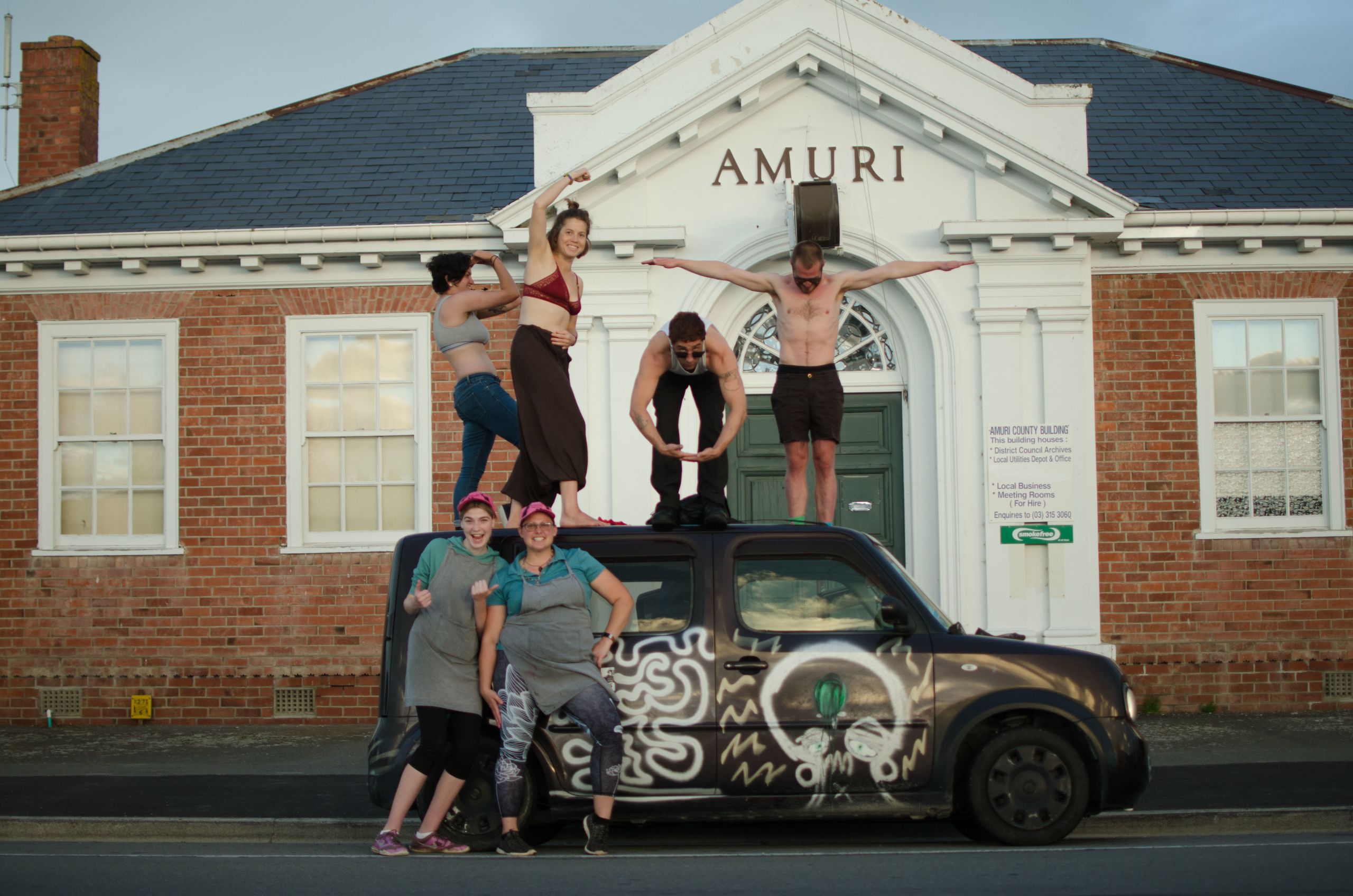 Shannon McIntyre, Nastya, Mikey Sperring, and Kyrill Masheka on top of Shannon's car in Culverden. Two Pussy Riot fans from the local fish and chilp shop pose in front.