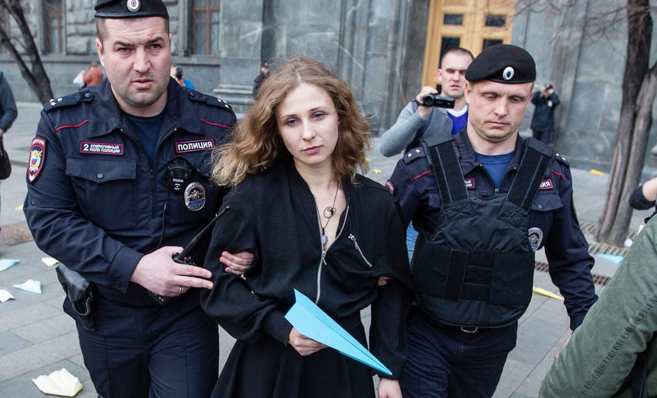 Masha escorted away by police after tossing paper aeroplanes at the Federal Security Services building in Russia.
