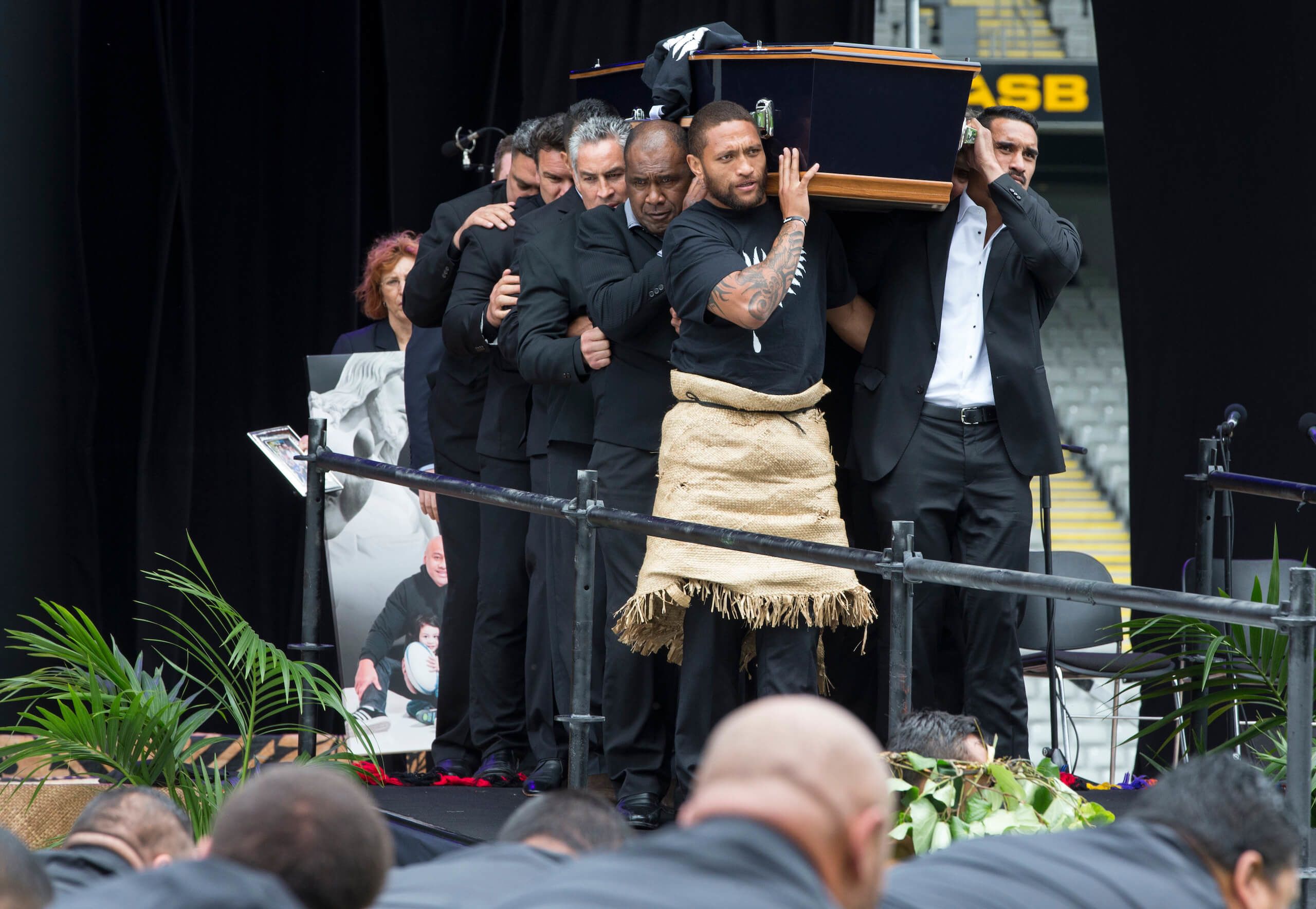 Pallbearers including Dylan Mika, Michael Jones, Frank Bunce, Joeli Vidiri, Manu Vatuvei , Jerome Kaino and others carry out the coffin of Jonah Lomu as former 1stXV team mates from Wesley College perform a haka in the foreground during the Jonah Lomu memorial service at Eden Park. Credit: Peter Meecham / Stuff