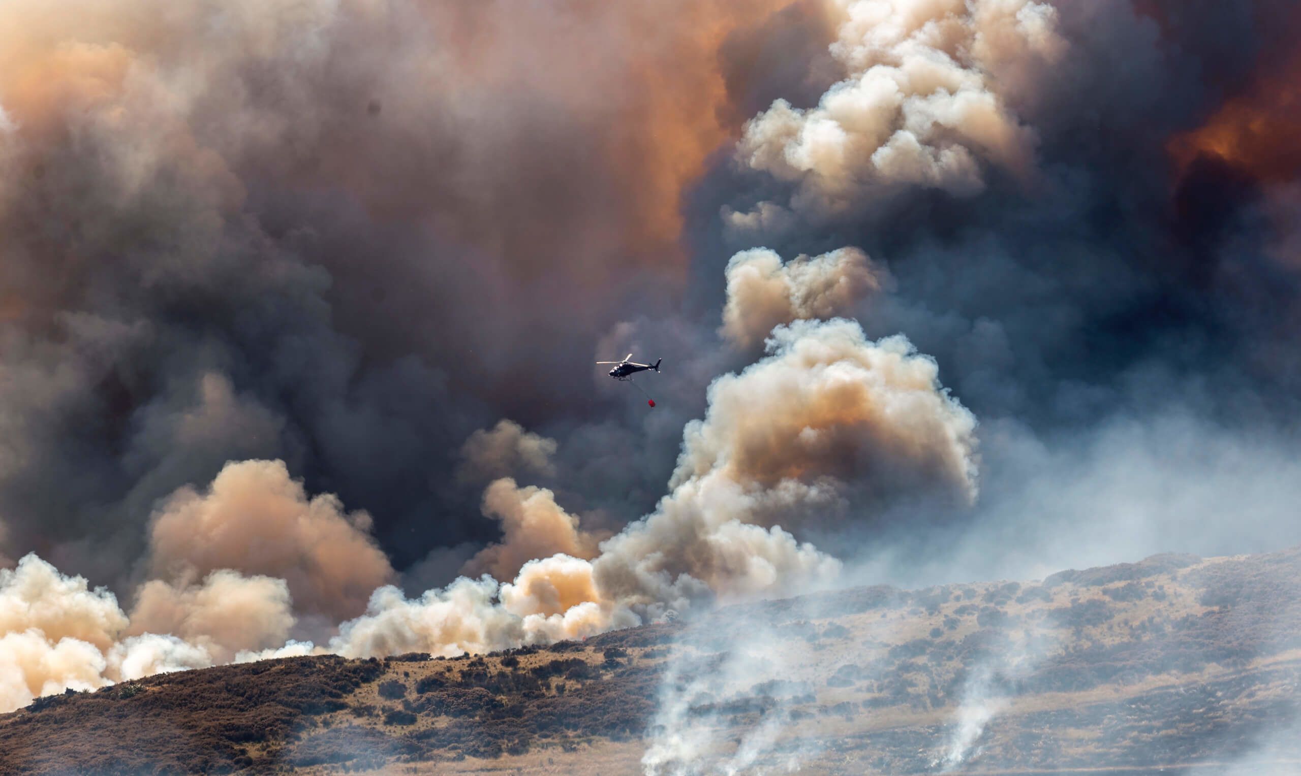 Helicopters with monsoon buckets fight the fire above Kennedys Reserve. Credit: John Kirk-Anderson / Stuff