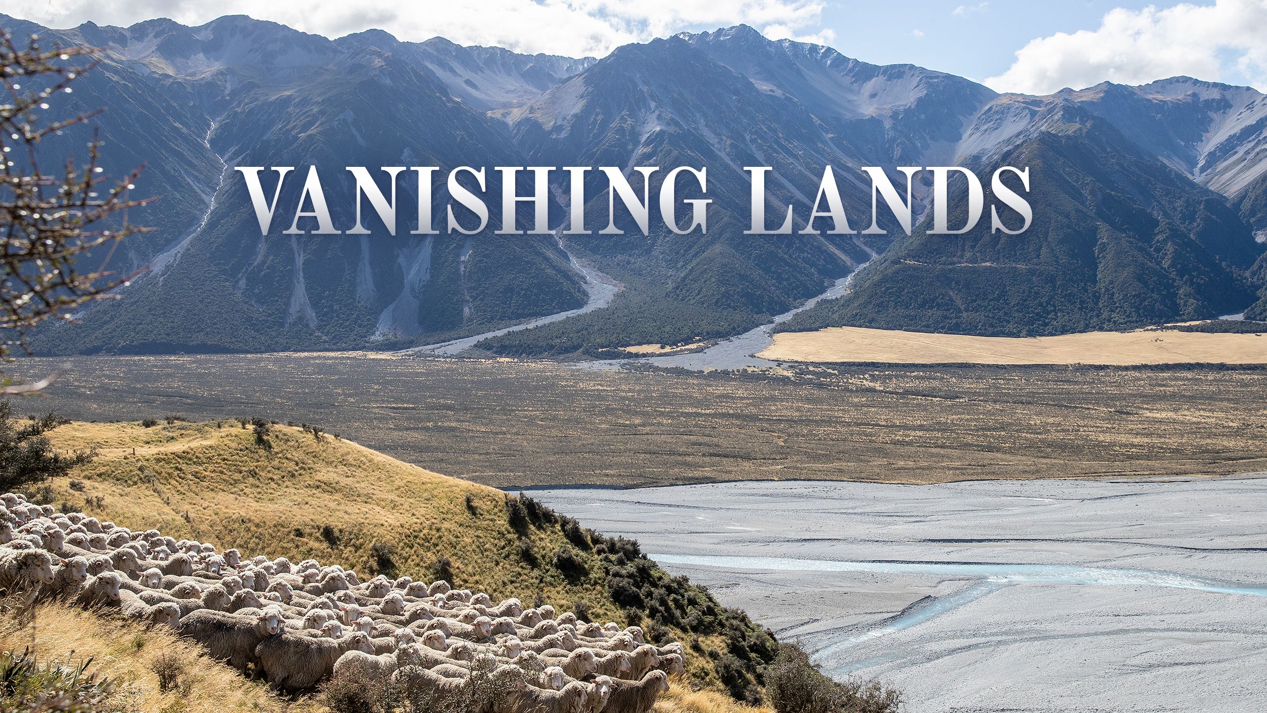 Vanishings Lands title image. Blue mountain range in the background and a flock of sheep gathering in the foreground on a hill overlooking an alluvial plain.