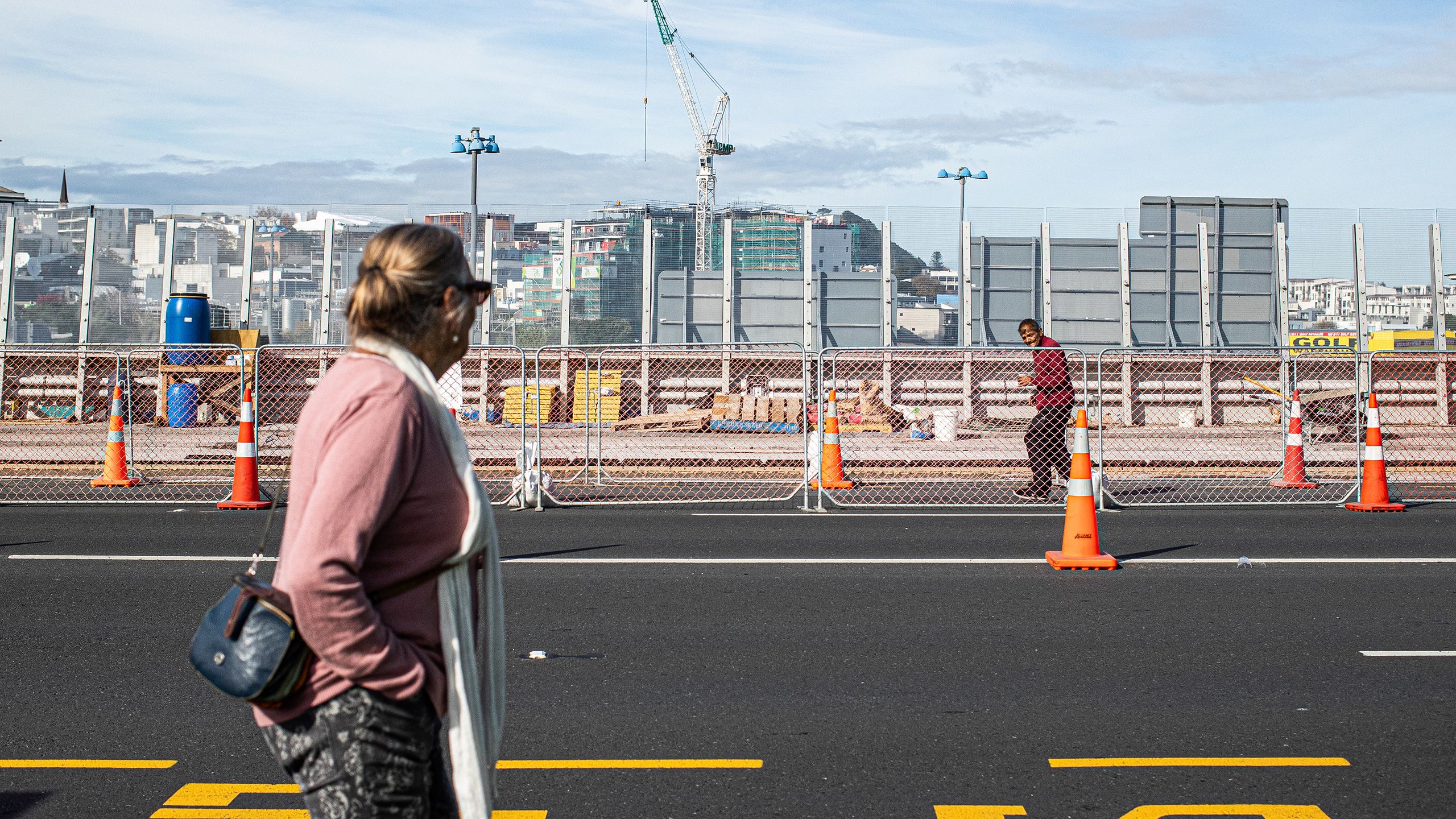 Woman walking right and man walking left across the Karangahape Road over bridge.