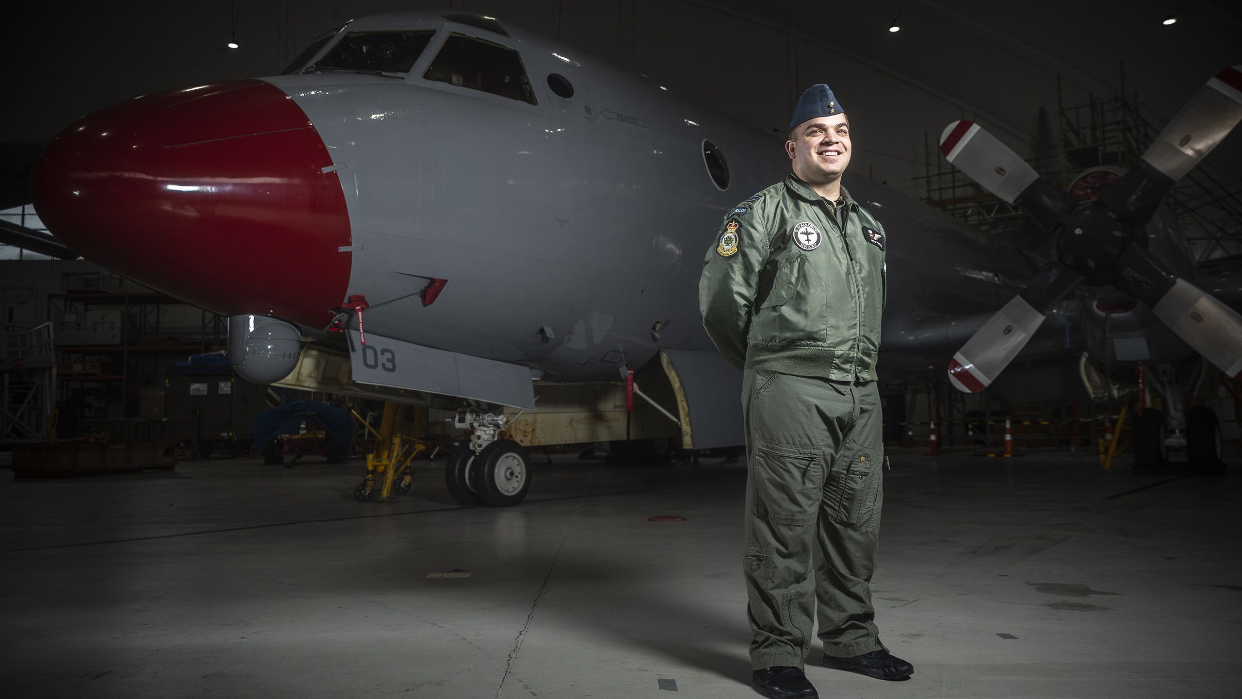 Hemi standing in uniforms in front of a military plane in a hanger.