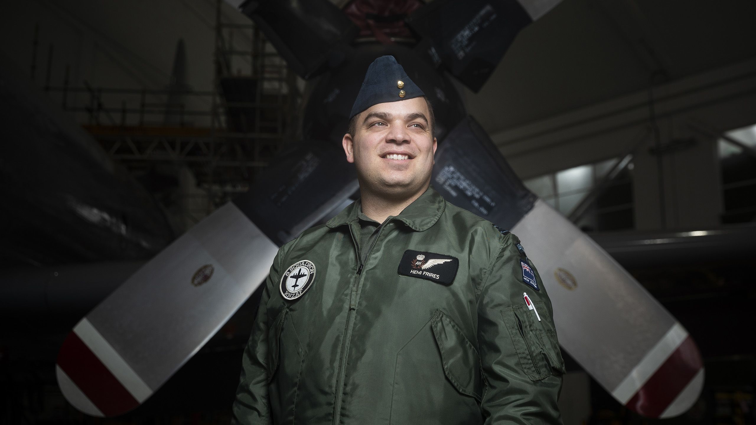 A smiling Hemi standing in front of large propeller wings of a military plane.