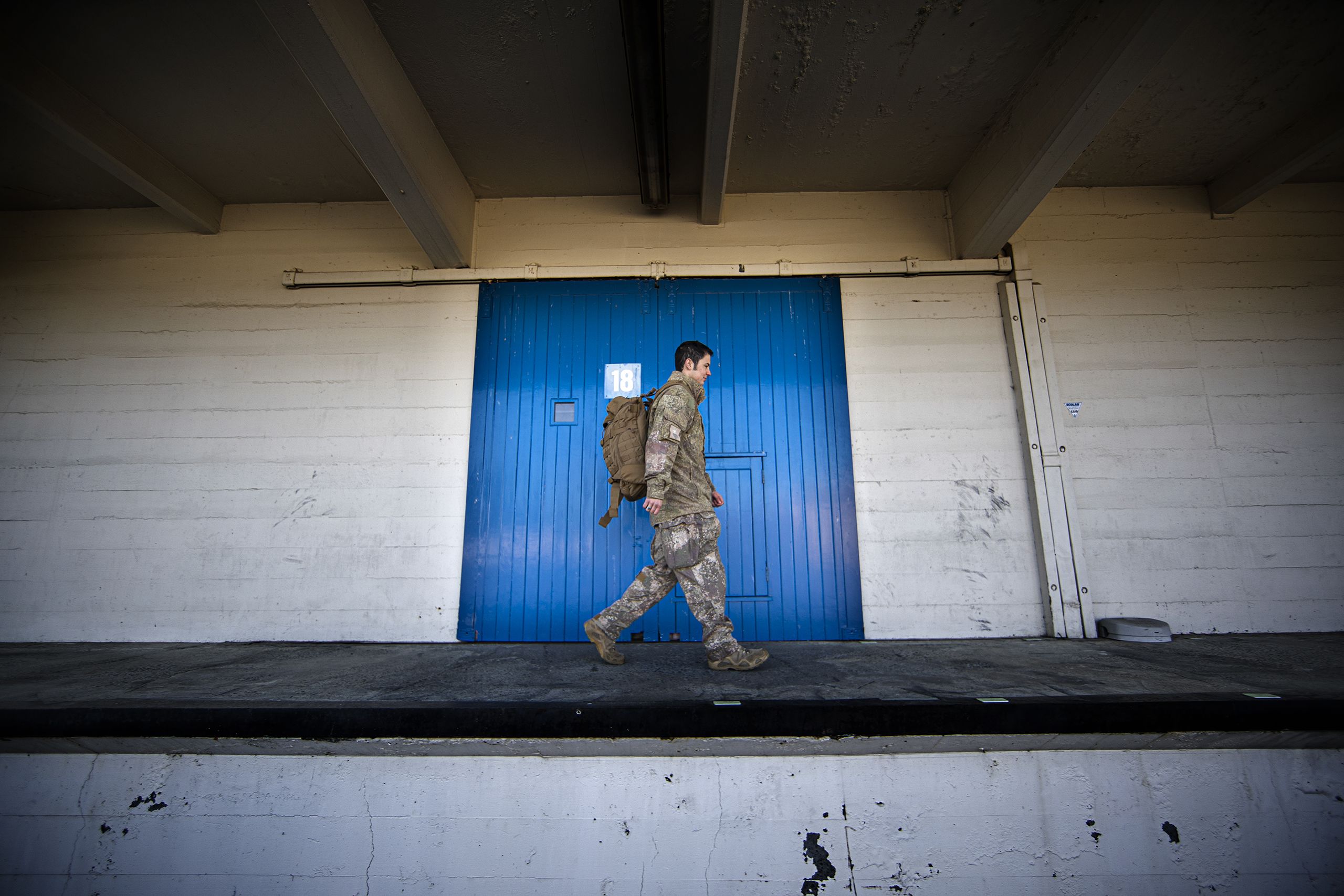 Wearing his army uniform, Sawyer walks along the path of a warehouse in from of a blue door.