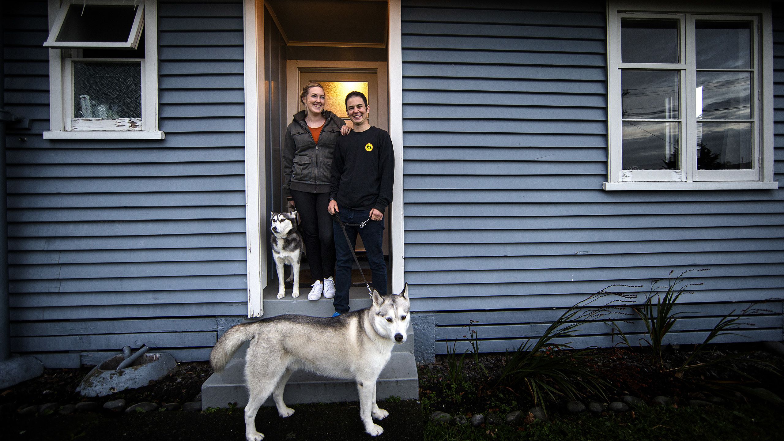 Sawyer and his partner, Penelope, stand on the steps at the door of their home with their two dogs, who wait to be taken for a walk.