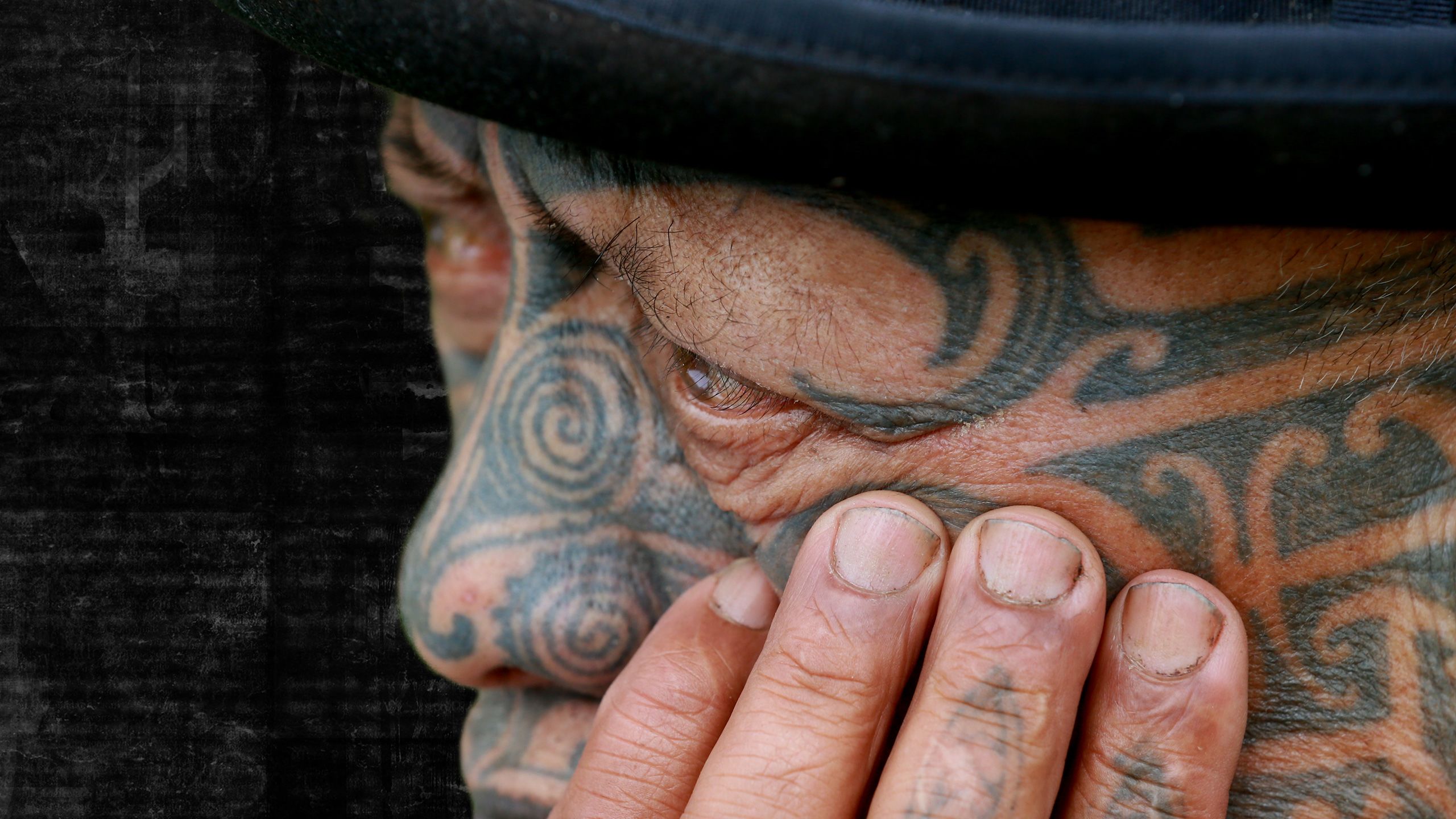 Close-up of Tame's face, hand on his cheek, looking pensive. Background changes to dark, newspaper texture.