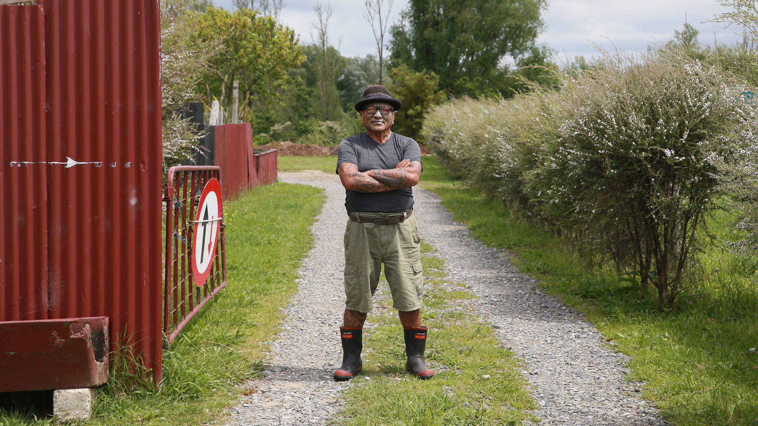 Tame Iti standing in his driveway, arms folded..
