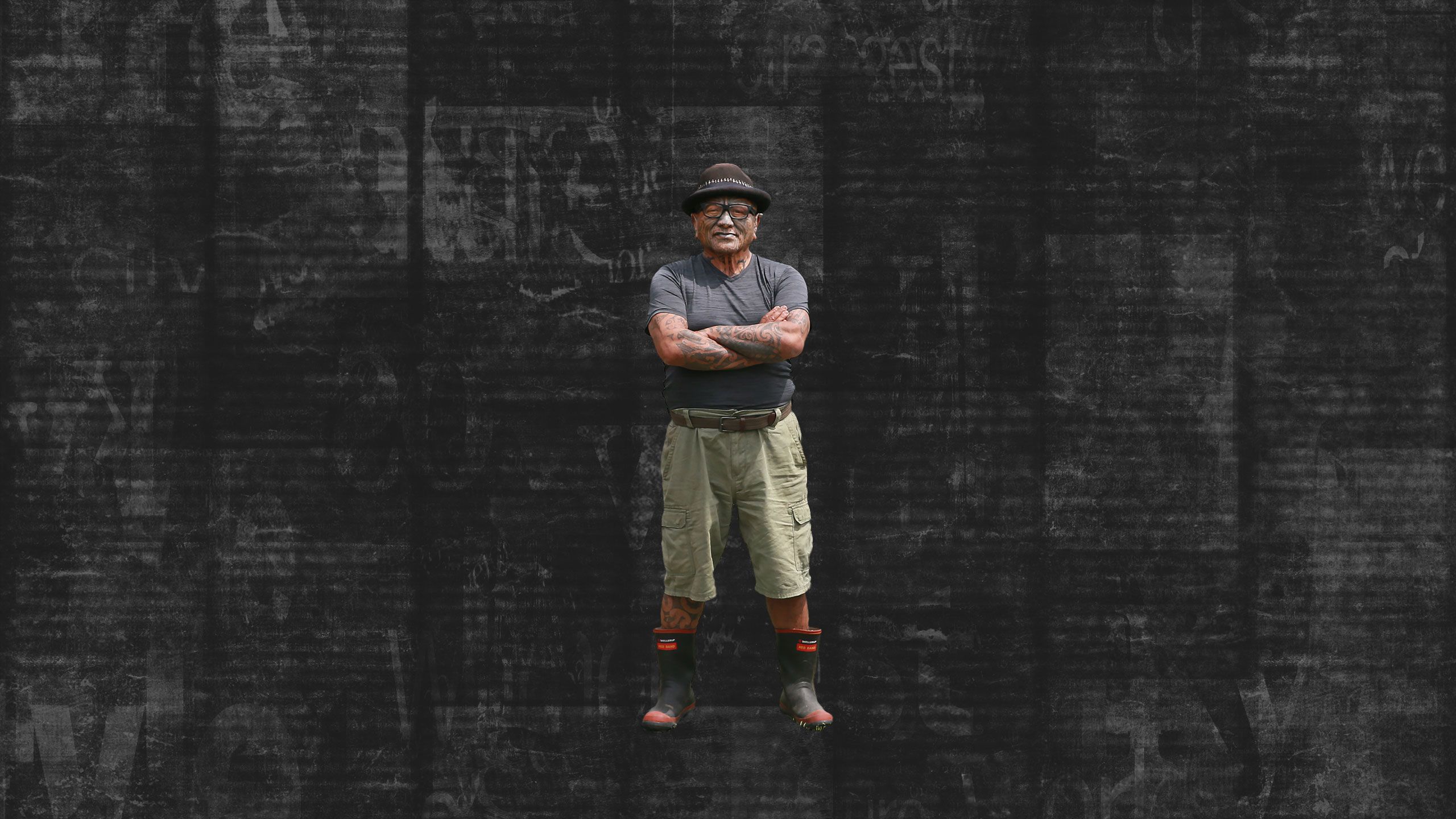 Tame Iti standing in his driveway, arms folded. Backgrounds turns into dark, textured newspaper background..