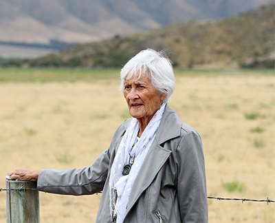 Waitaha Tumuaki Anne Te Maihāroa-Dodds, resting her hand on a fence post before an expanse of grassy land, looks off into the distance.