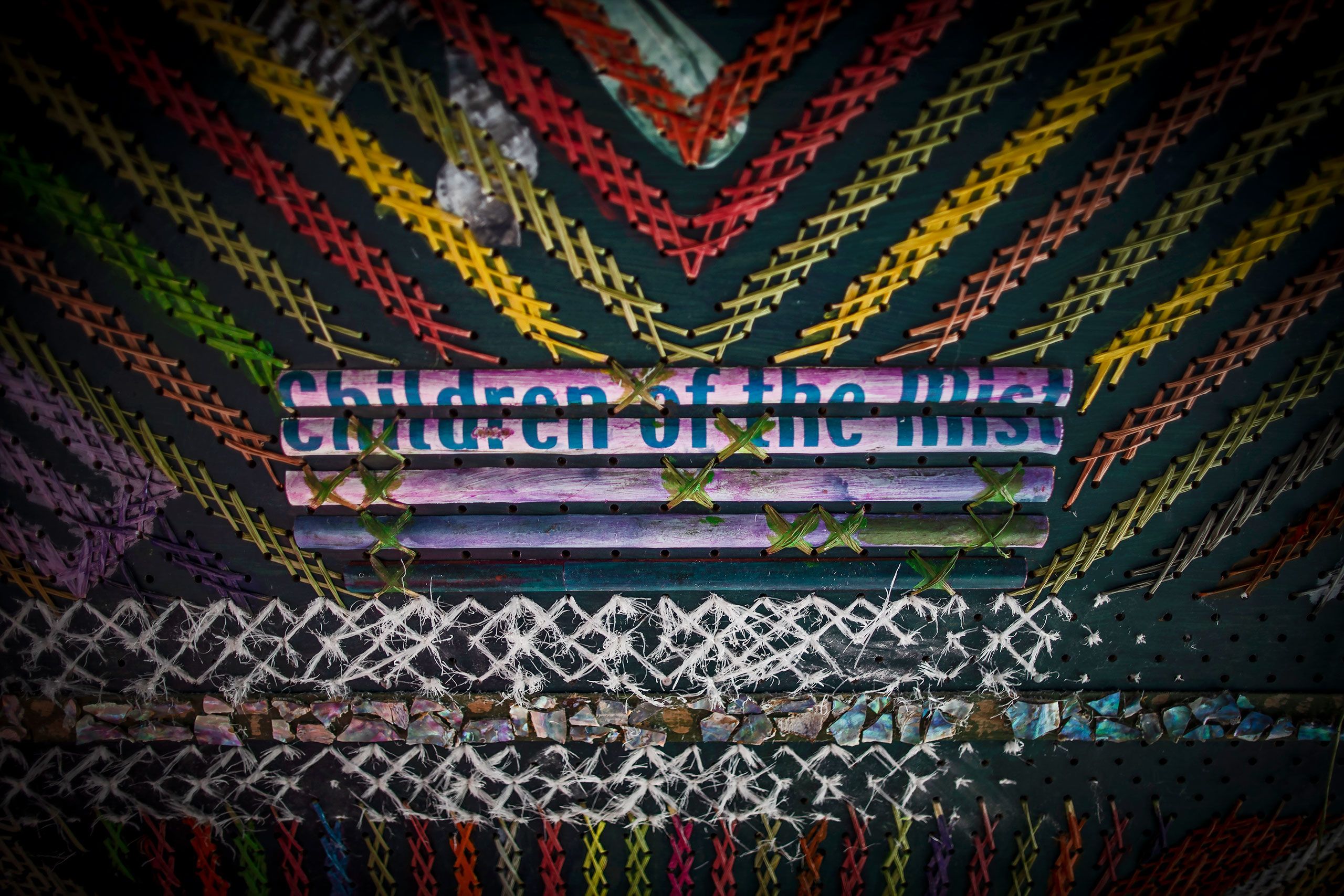 Detail of one of Tineti's colourful tukutuku wall panels with a hand-written sign, saying "Children of the Mist".