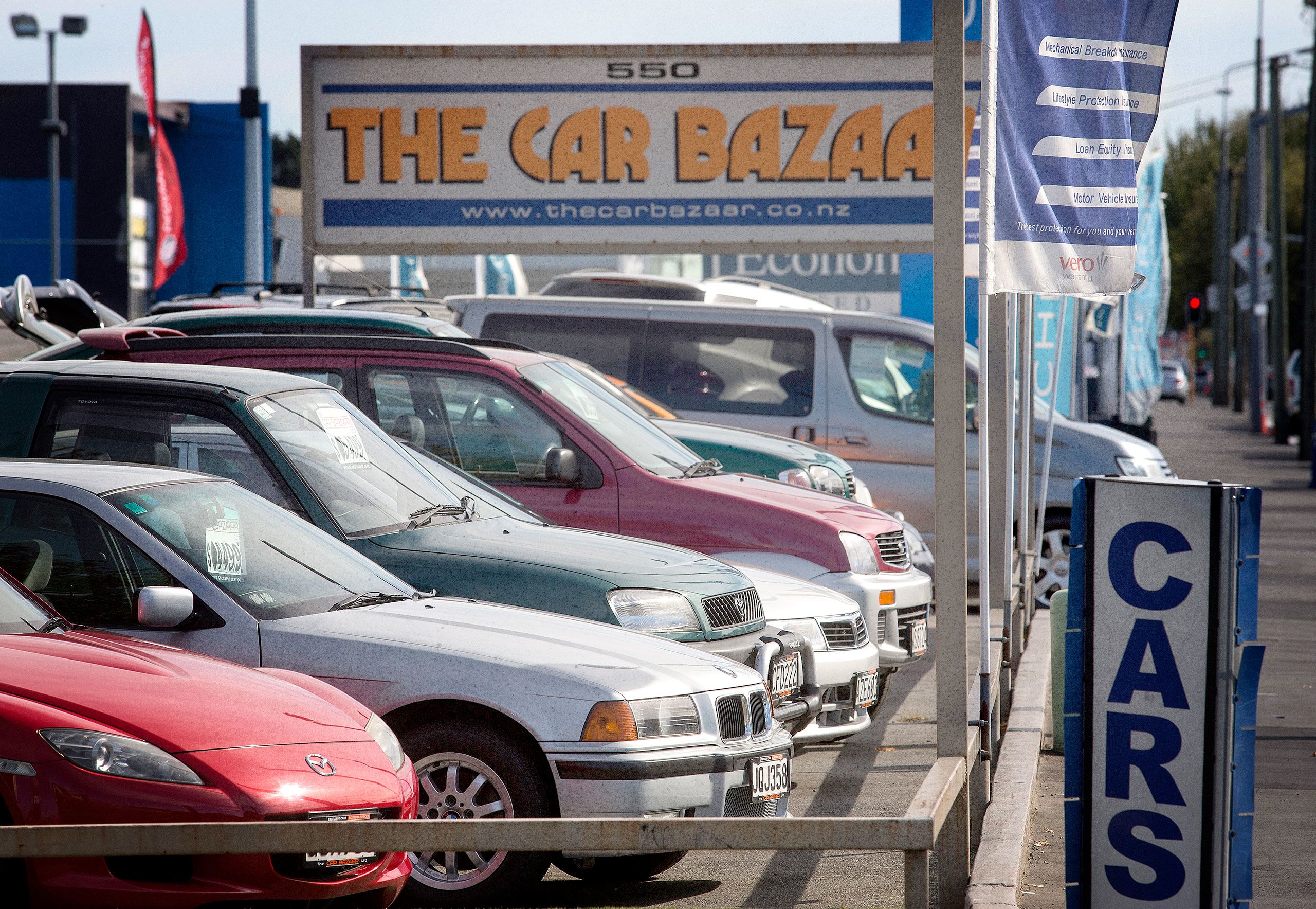 Cars line the front of a sale yard, with a sign saying 'The Car Bazaar' in the background.