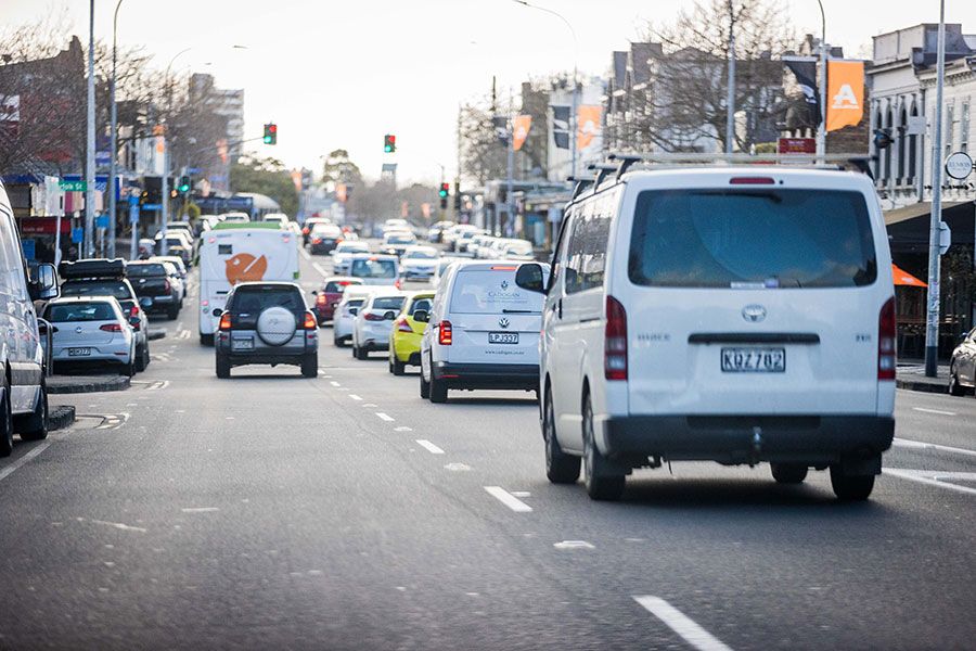 An urban street is bustling with traffic, including vans and a bus.