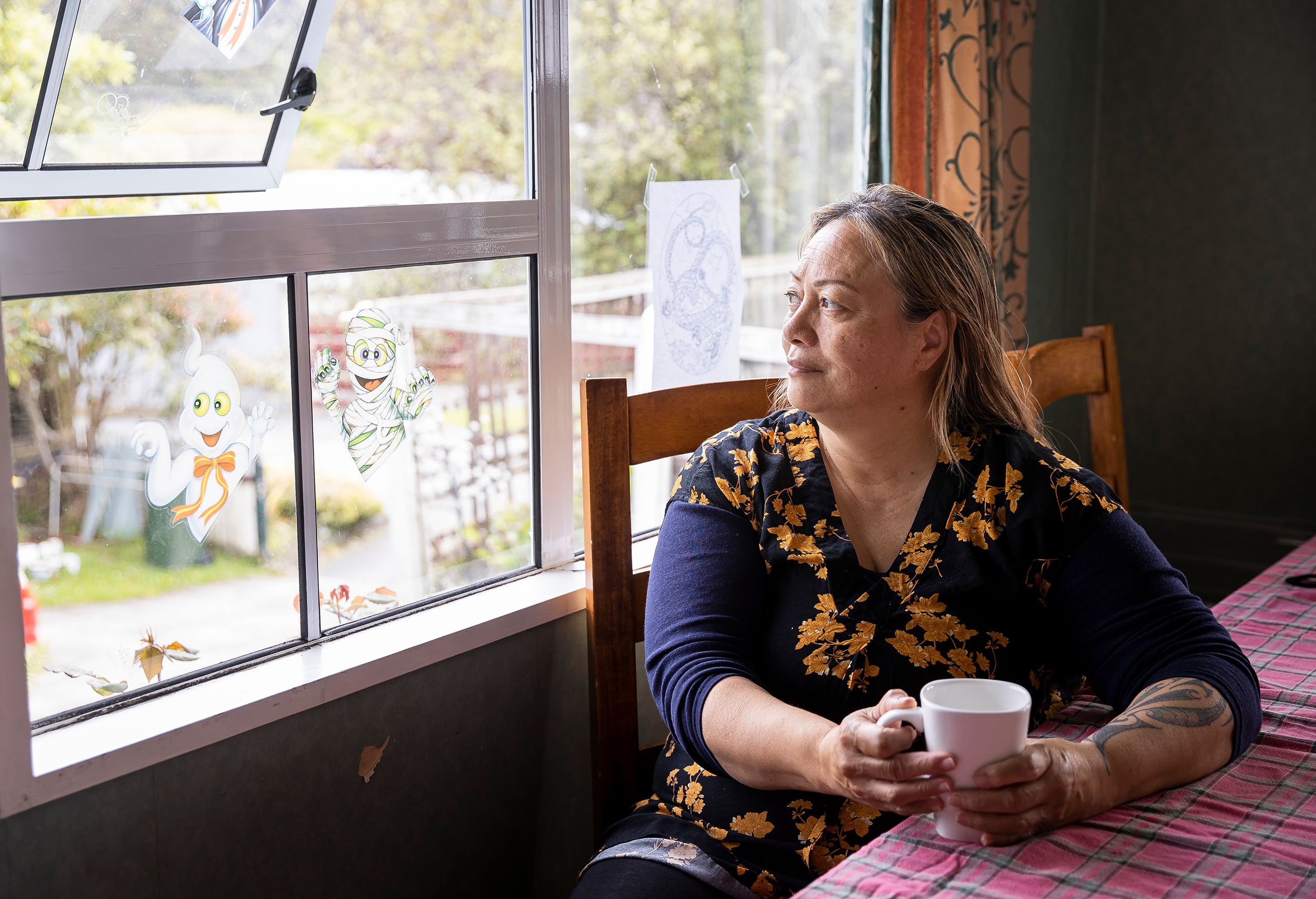 Tania sitting at a table with a coffee cup, looking out the window.