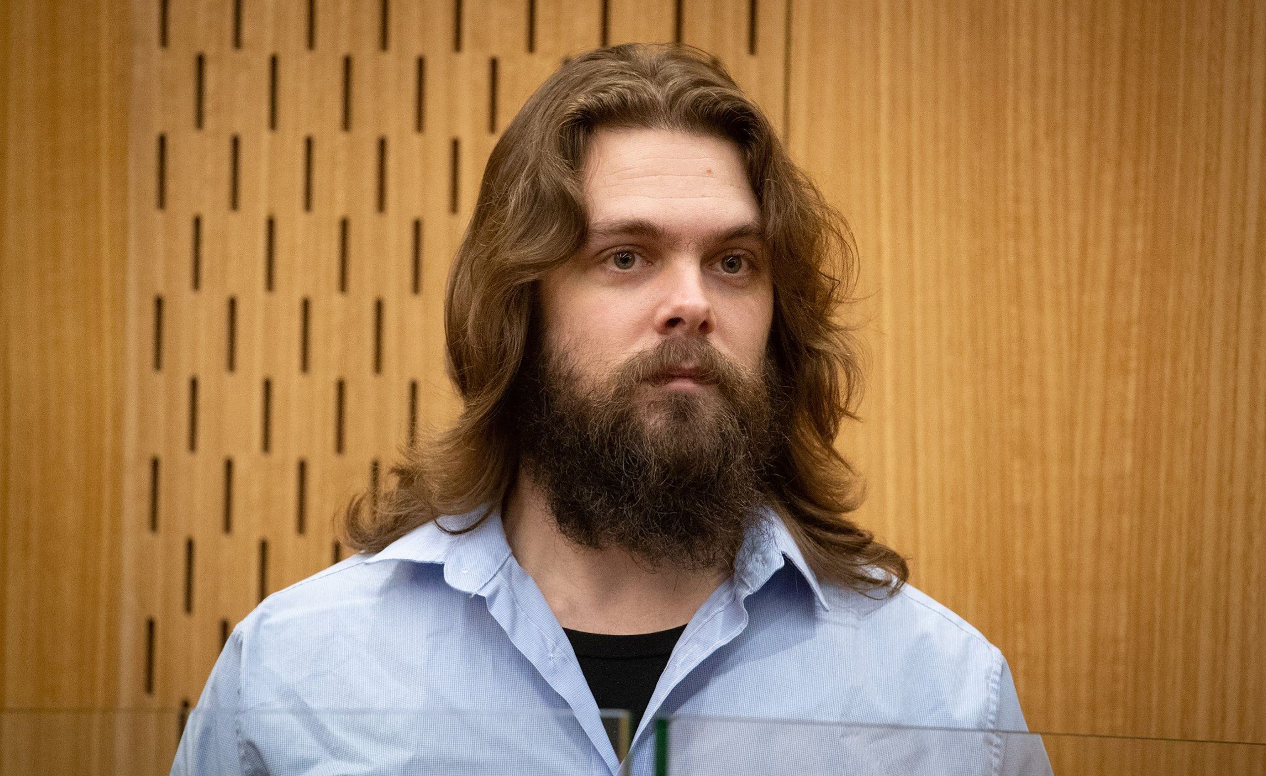 Tristan Locke in court, wearing a collared shirt. He has longish hair.