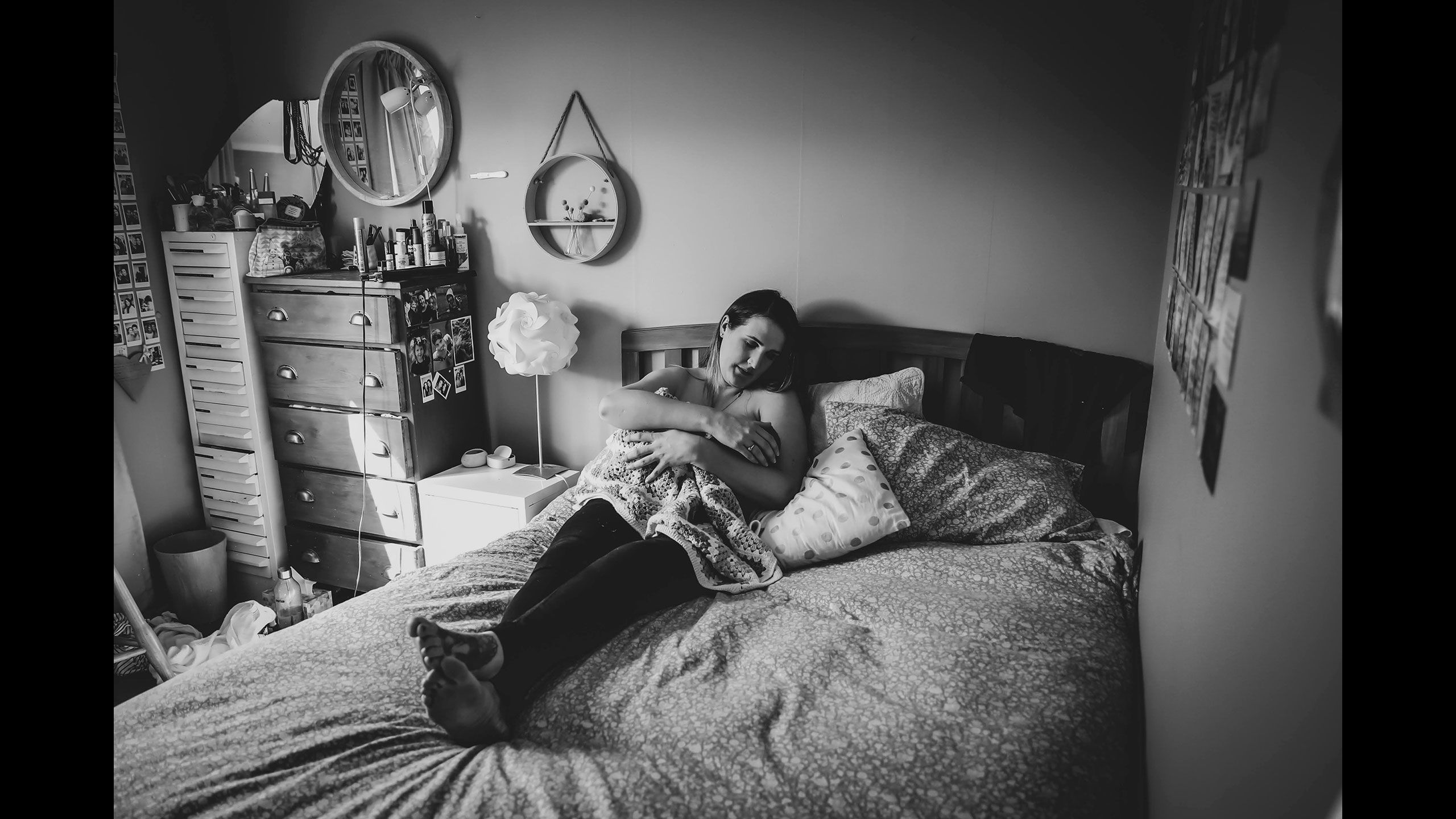 A black and white image of Jessica lies on her bed in her bedroom breastfeeding Hazel who is in her arms.