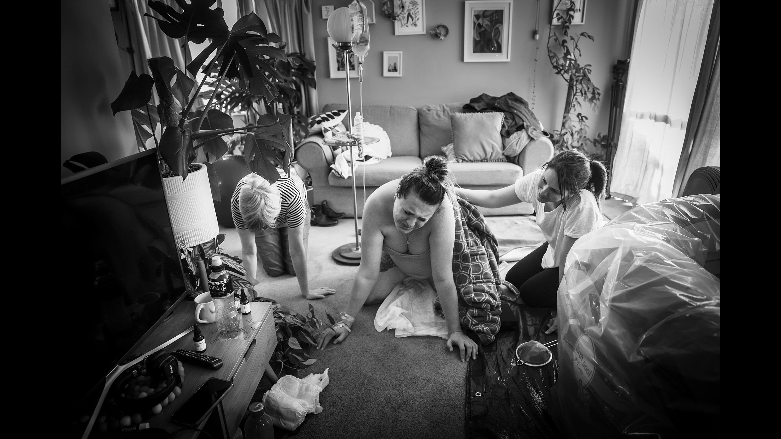Jessica kneels in her front room trying to push with her mother keeling next to her to the left and her sister-in-law kneels on the right rubbing Jessica's back.
