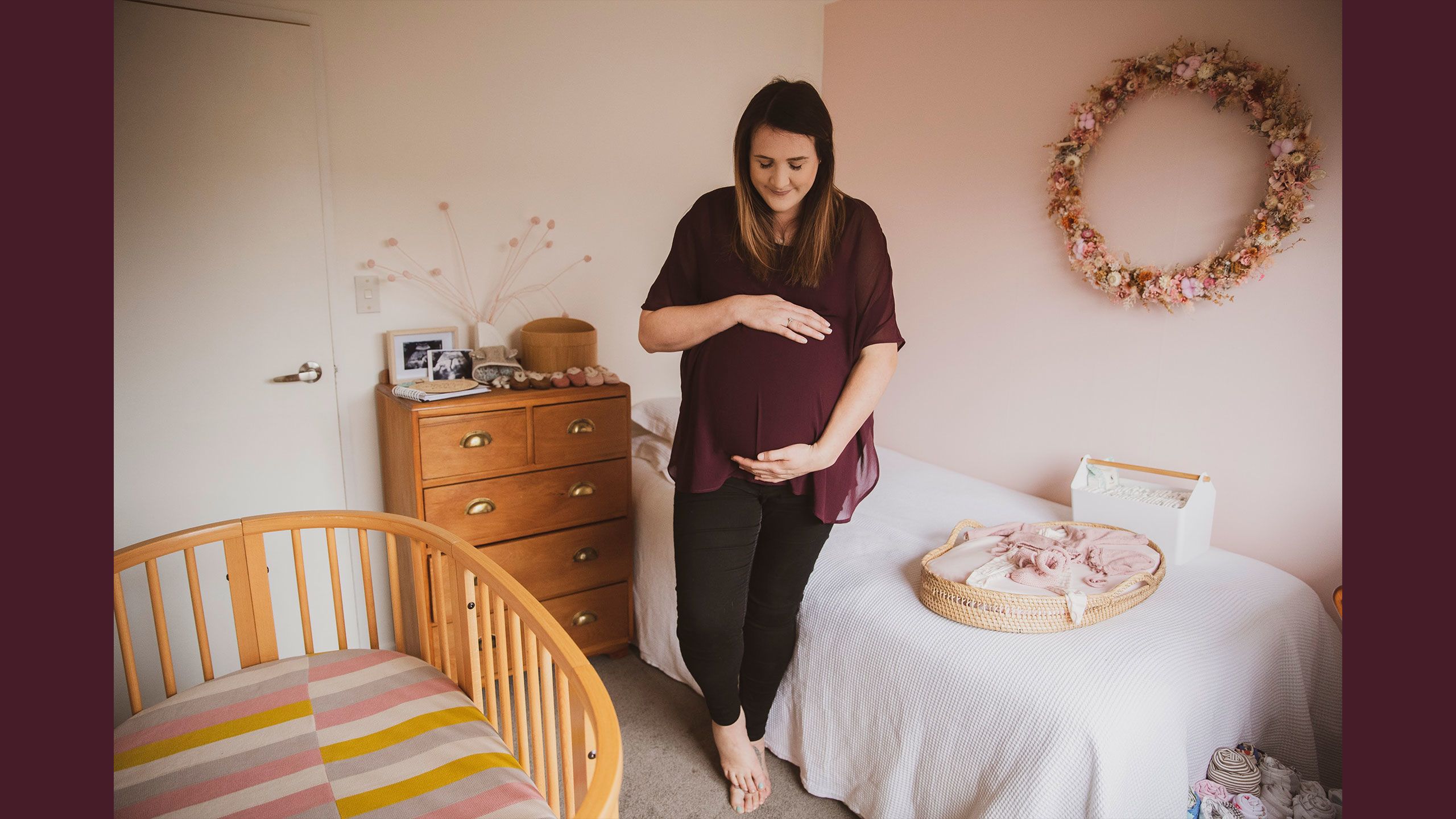 Jessica stands in her light salmon pink coloured nursery bedroom holding her baby bump.