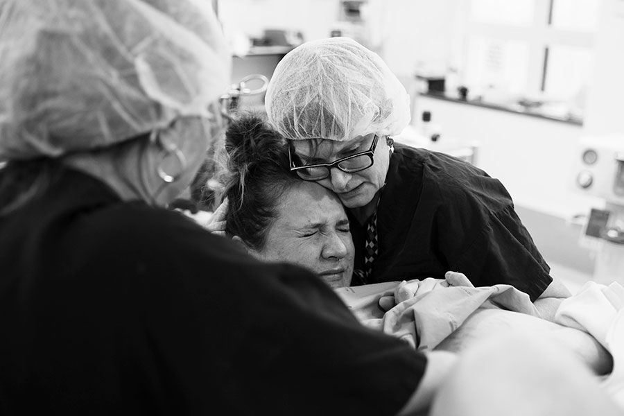 Jessica at the hospital pushing during labour. The midwife holds her hand and rests her cheek on Jessica's head. 