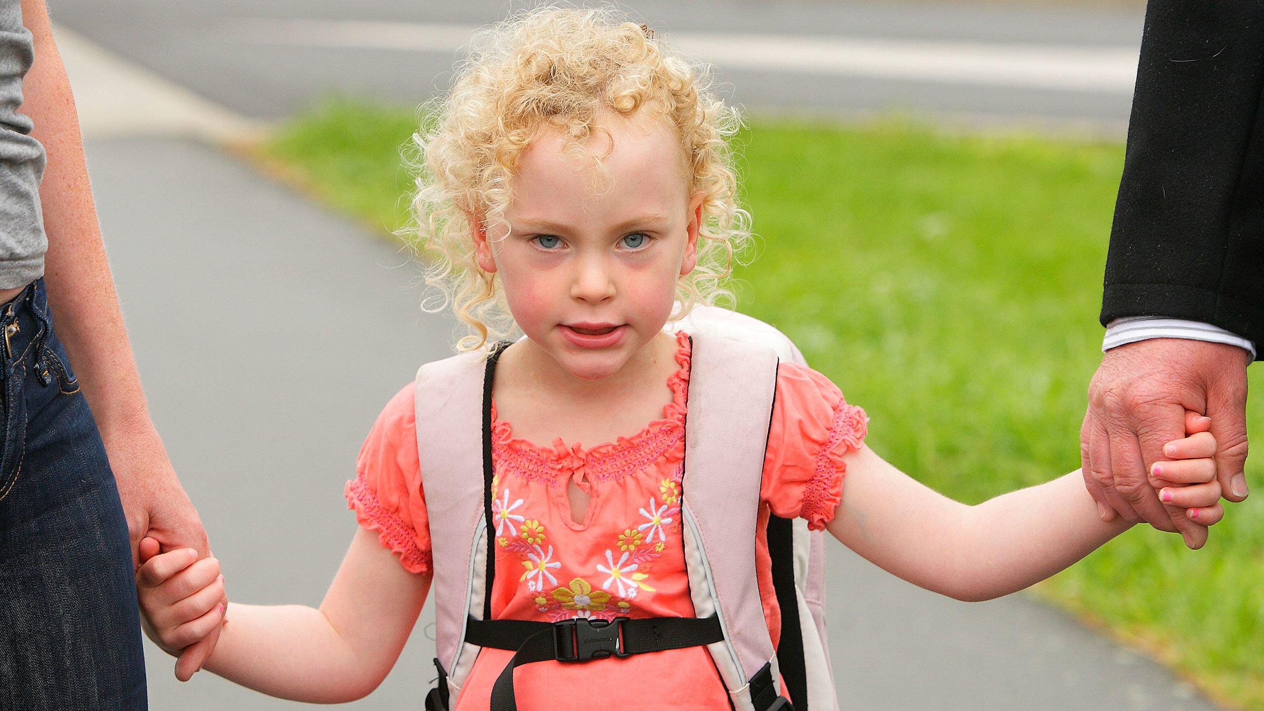 Charlotte as a youngster walking with her parents holding their hands on either side.