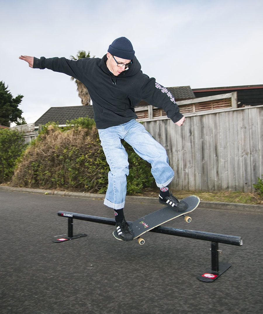Cullen skateboarding. He wears a black beanie hat and sweatshirt, pale blue jeans and black and white trainers.