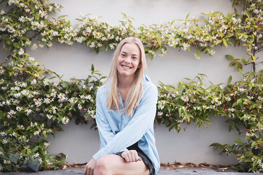 India, now fully grown, sits on a bench with a Jasmine plant climbing on the wall behind her.