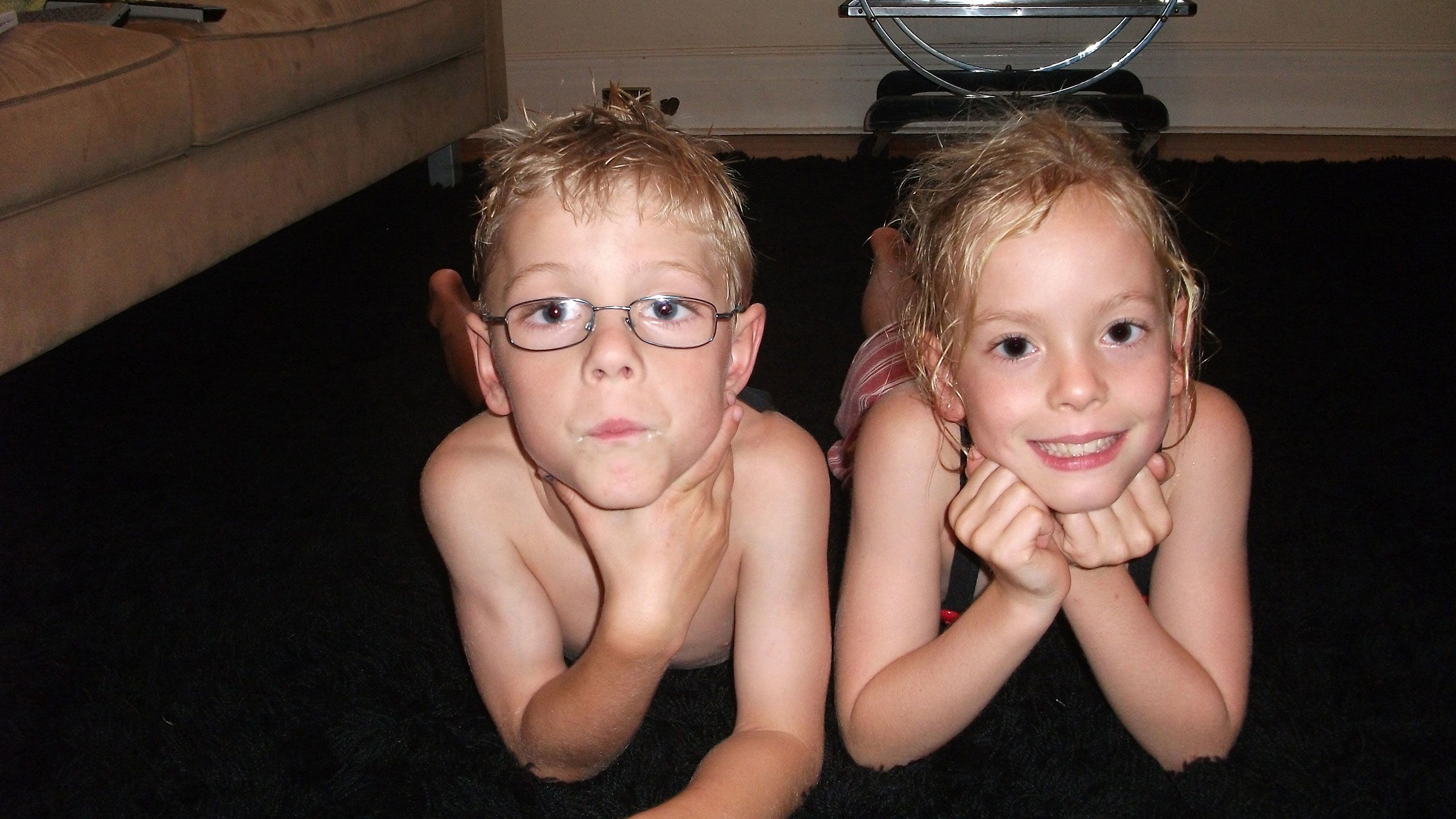 Mac and India lie on their fronts looking directly into the camera. They are both wearing togs and their hair is wet from swimming.