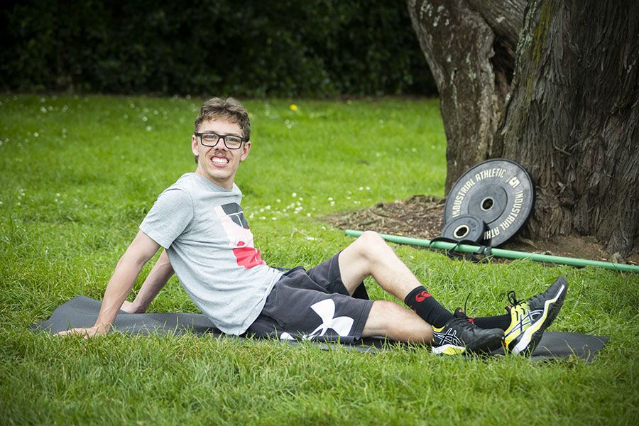 Mac lies on a gym mat in the park with his weights nearby.