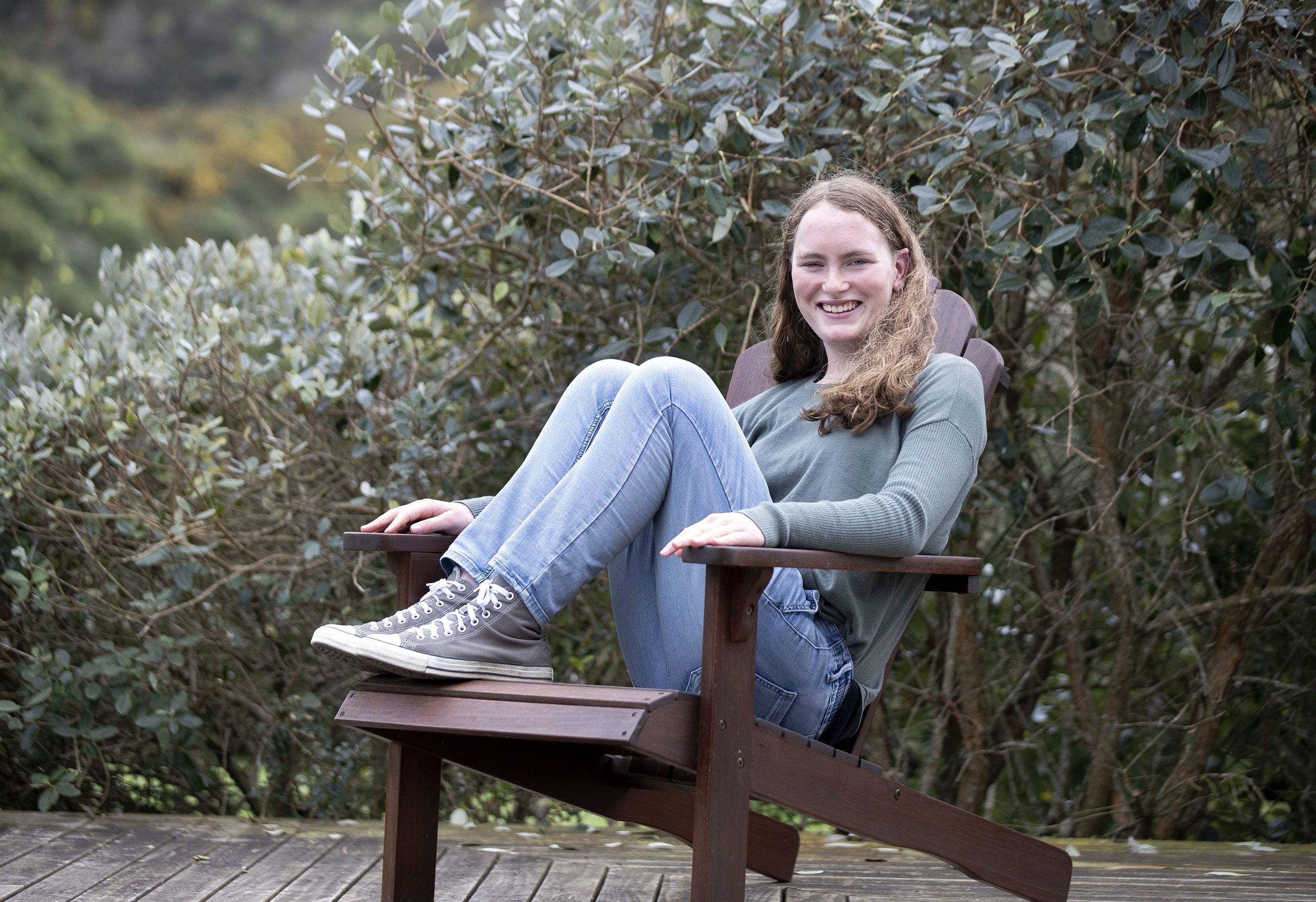 Charlotte, now a young adult, sits with her legs bent up on a deck chair at her home.