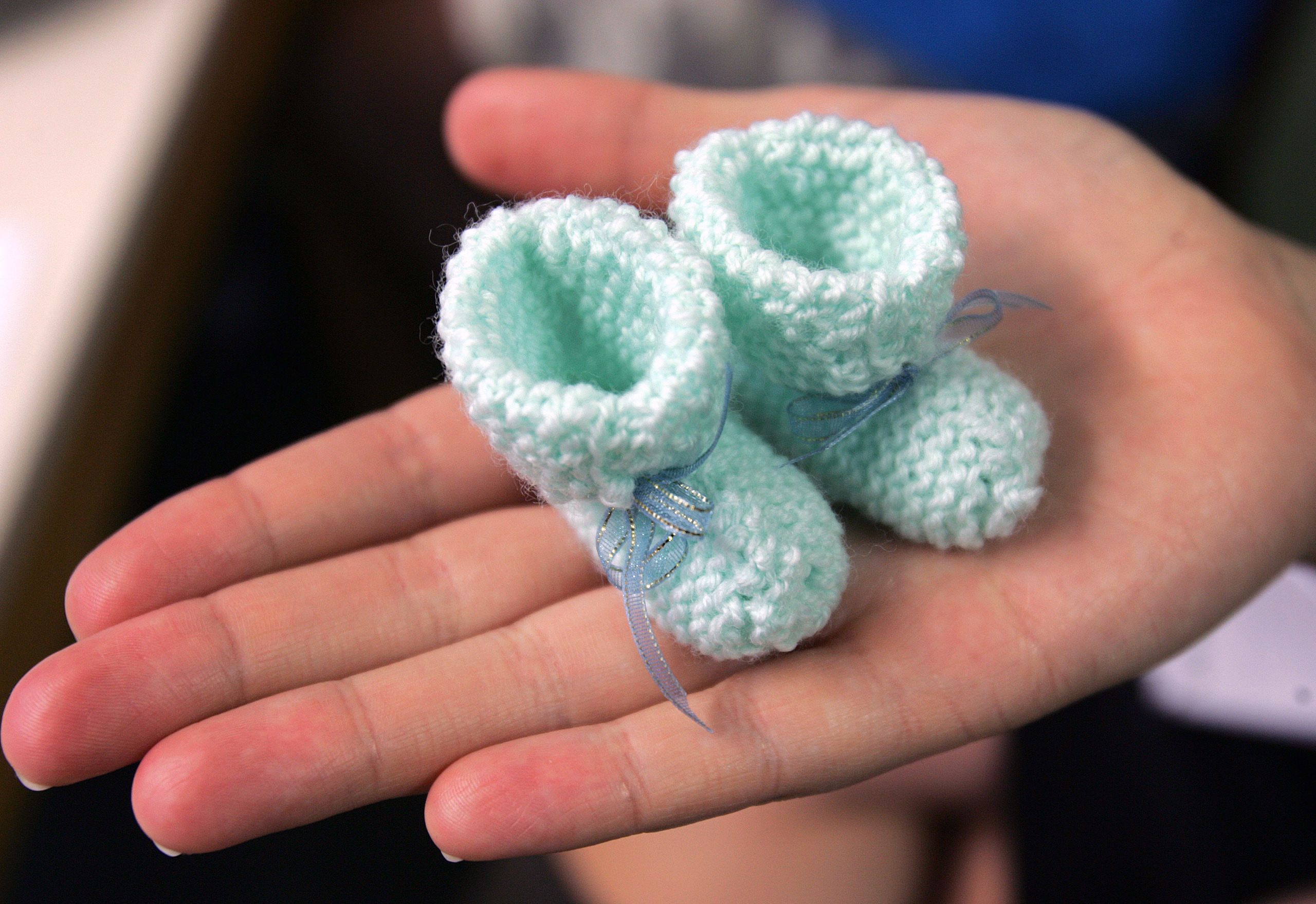 A hand holding tiny pale green booties.
