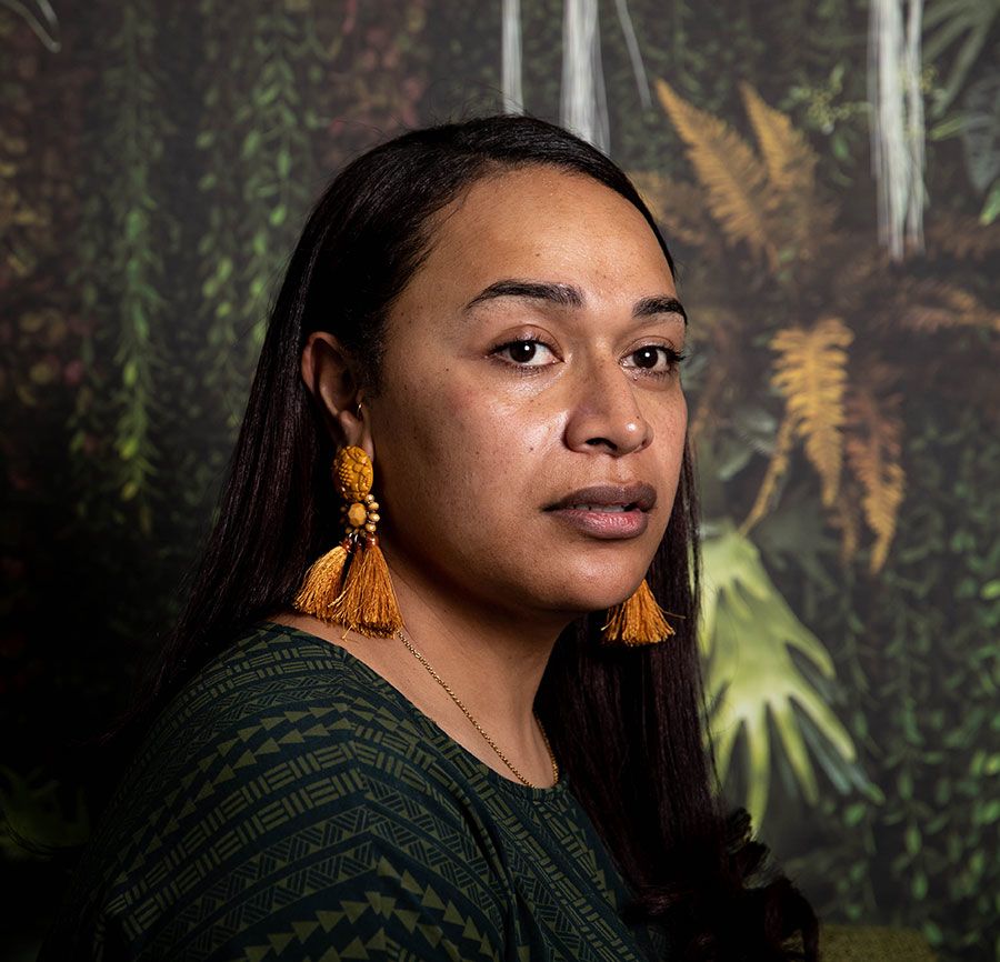 Amanaki in front of the tropical forest wallpaper, gazing into the distance. Her deep brown hair is worn loose and straight.